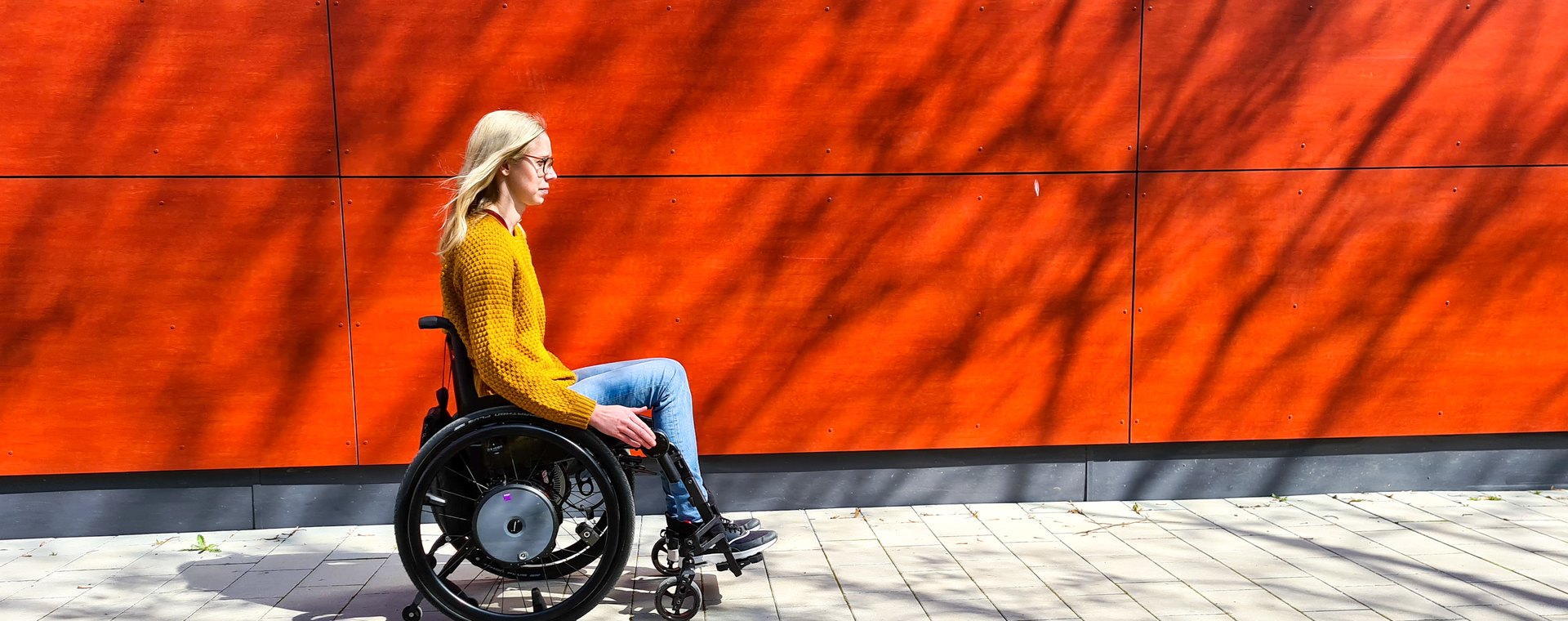 Frau im Aktivrollstuhl mit Alber e-motion Zusatzantrieb, unterwegs auf dem Gehweg