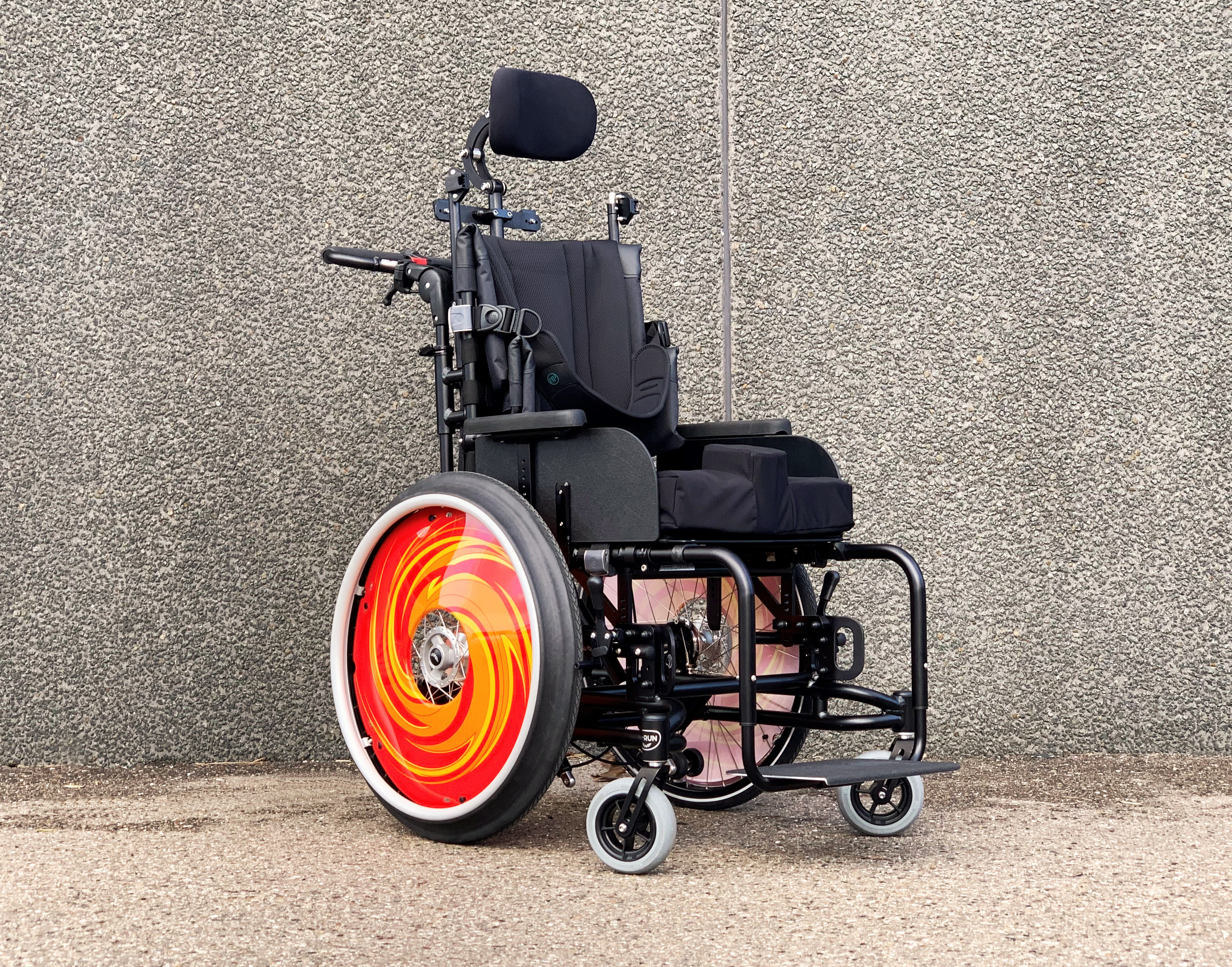 Wolturnus A-Run Comfort mit stufenlos geneigtem Sitz und orangefarbenem Speichenschutz vor einer Betonwand