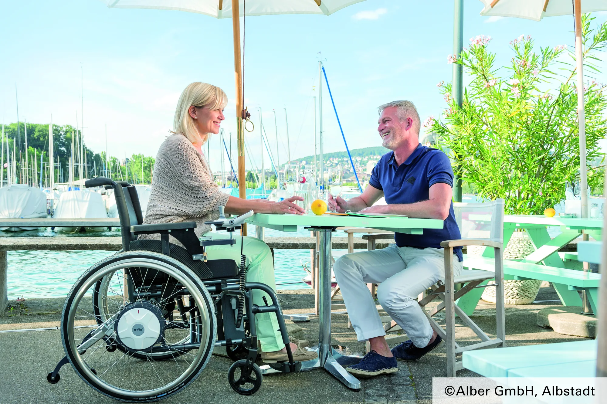 Rollstuhlfahrerin mit e-fix am Tisch im Freien