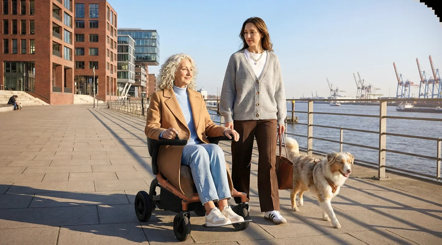 Frau fährt den Alber erivo carbon R20 über eine Hafenpromenade, eine Begleiterin mit Hund geht daneben