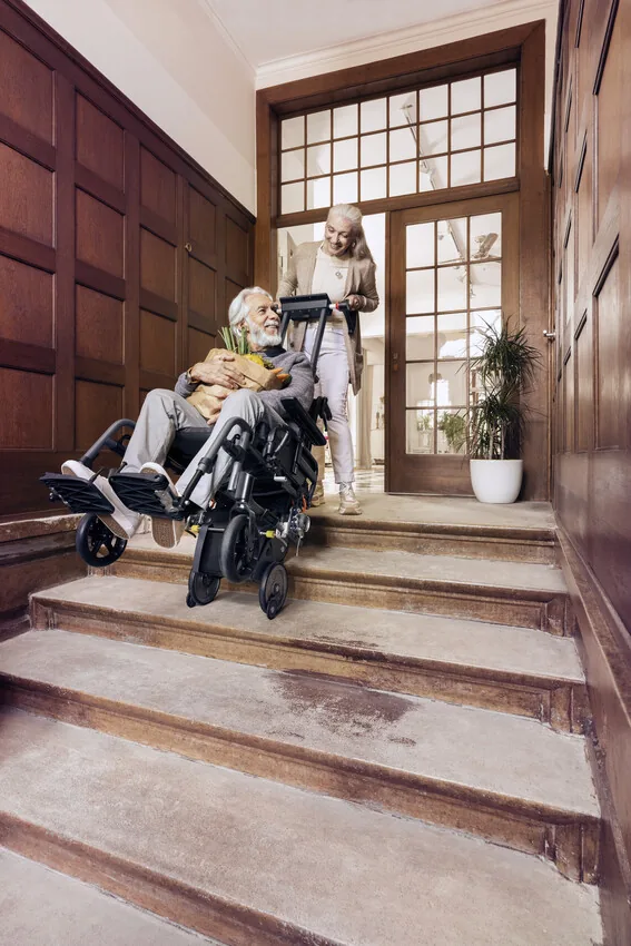 Begleitperson fährt mit dem Alber scalamobil S45 und einem Rollstuhl eine Treppe im Wohnhaus hinauf