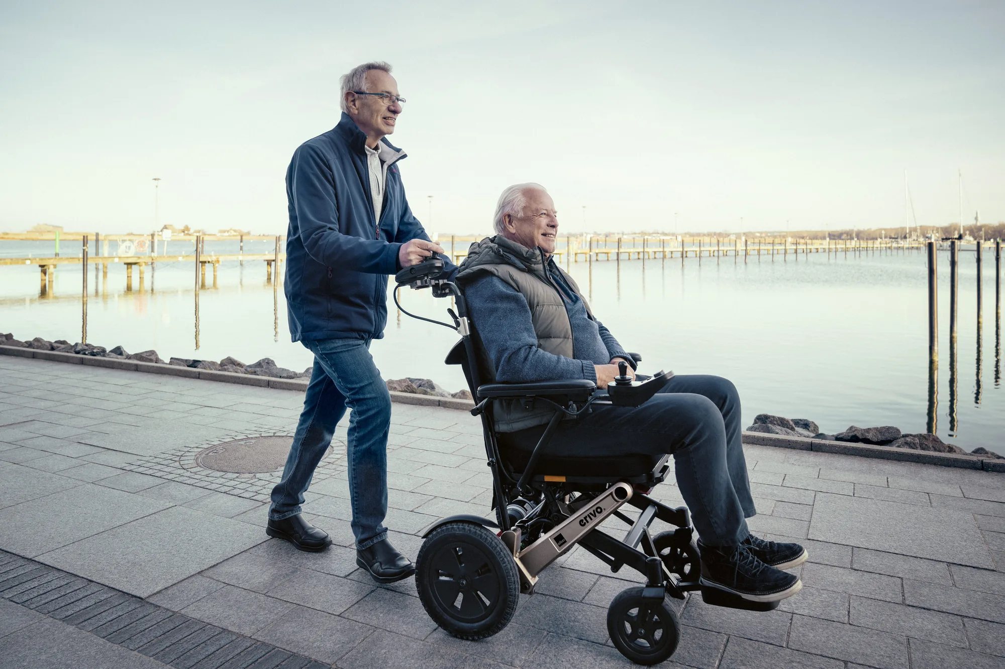 Zwei Männer an einer Wasserpromenade, einer sitzt im Alber erivo Elektrorollstuhl